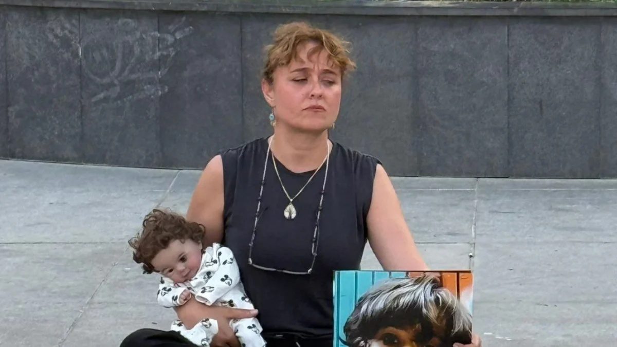 Yasemin Minguzzi adliye önünde eylem yaparken, elinde oyuncak bebek ve çocuğunun fotoğrafı ile oturuyor #gazetegezegen